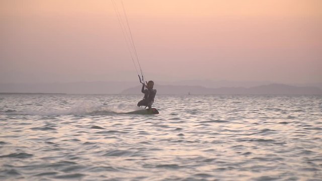 Kite surfer is gliding on water during sunset, orange and purple sky, Egypt