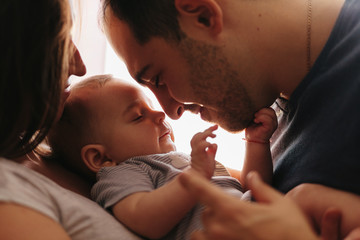 Baby with his parents playing on the bed. Happy family at home. Lifestyle cozy photos. Little boy 4...