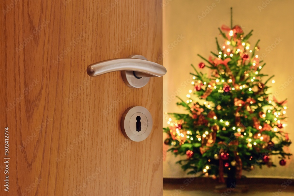 Sticker half opened door into the cozy home interior with beautiful christmas tree - blured lights