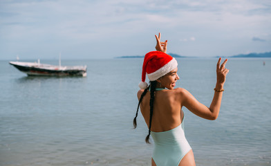 Girl in a swimsuit and New Year's hat on the ocean on a tropical island.