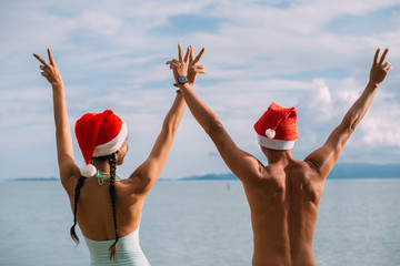 Young couple rejoice in Christmas caps on the ocean on a tropical island.
