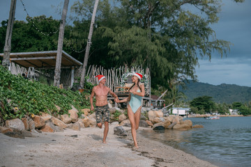A young couple rejoices in Christmas caps on the ocean on a tropical island.