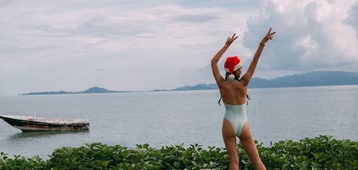 Girl in a swimsuit and New Year's hat on the ocean on a tropical island. banner