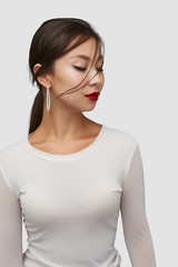 Medium shot of a young Asian woman in an ivory white blouse and with a white stud earring made as...