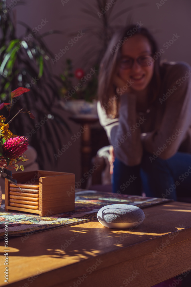 Wall mural Woman talking to voice controlled smart speaker in a living room. 