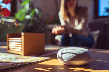 Woman talking to voice controlled smart speaker in a living room. 