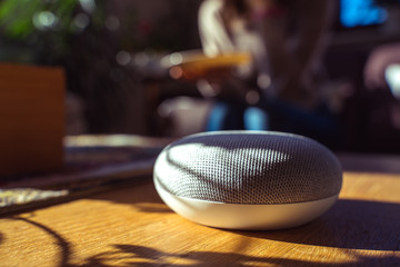 voice controlled smart speaker with a woman woman in the background in a interior home environment. Smart AI speaker concept 