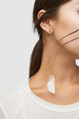 Cropped close-up shot of a brunette woman in an ivory white top and with a stud earring with long golden chains with dangling white fabric feather and nacre disc. 