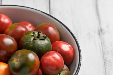 Black prince tomatoes and yellow tomatoes in enamel bowl on white wooden table. Close-up, blurry background