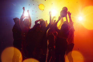 Memories. A crowd of people in silhouette raises their hands on dancefloor on neon light...