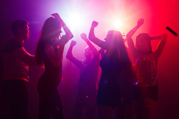 Jam session. A crowd of people in silhouette raises their hands on dancefloor on neon light background. Night life, club, music, dance, motion, youth. Purple-pink colors and moving girls and boys.