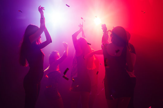 Celebrating. A crowd of people in silhouette raises their hands on  dancefloor on neon light background. Night life, club, music, dance,  motion, youth. Purple-pink colors and moving girls and boys. Photos |