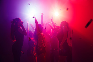Bass. A crowd of people in silhouette raises their hands on dancefloor on neon light background. Night life, club, music, dance, motion, youth. Purple-pink colors and moving girls and boys.