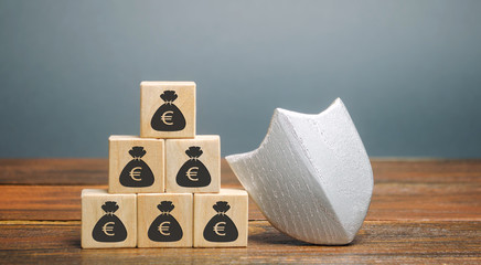 Wooden blocks with money and protection shield. Concept security of money, guaranteed deposits. Client rights protection. Compensation for losses in inflation, safeguarded investment capital.