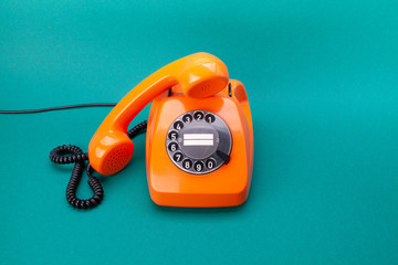 Retro phone orange color, plastic handset receiver on green background.