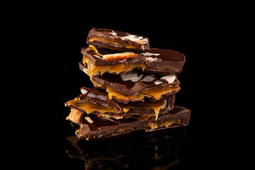 Heap of chopped handcrafted chocolate with dried oranges and caramel filling isolated on black