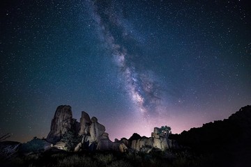 Beautiful shot of silhouettes of rocks under the purple sky full of stars - perfect wallpaper - Powered by Adobe