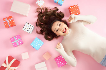 Young Asian excited woman lying on pink floor with many colorful gift boxes. Top view. - Powered by Adobe