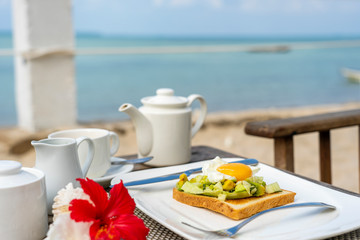 Healthy sandwich with avocado, cucumber and poached eggs on table for healthy breakfast on the beach near sea. Food and breakfast concept.