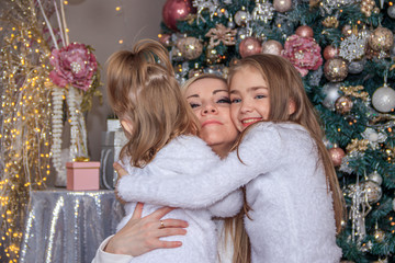 Mom and daughters at the Christmas tree. Christmas season. Sisters. Merry Christmas and happy holidays Cheerful mom and her cute daughters exchange gifts.