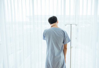 Patient asian man 25 year old Wear a sick suit feeling unwell and worry,stand at room. Asian patient young male 25s is a flu feel not good back Standing facing the window in the room.white background