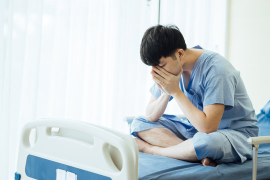 Patient Asian Sad Man 25 Year Old Wear A Sick Suit Feeling Unwell And Worry, Sit In A Bed At Hospital. Asian Patient Young Male 25s Is A Flu Feel Not Good Strain Sit On A Bed In The Room. 