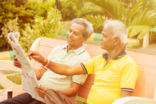 Two happy senior men reading newspaper at park outdoor - elderly friends enjoying moring news - Concept of happy older men lifestyle.