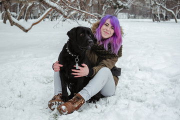 A young woman plays with her pet black Labrador outside in winter.