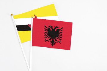 Albania and Brunei stick flags on white background. High quality fabric, miniature national flag. Peaceful global concept.White floor for copy space.