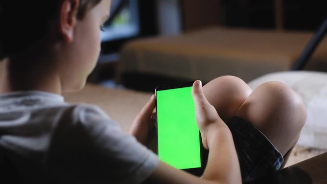 child stares into a smartphone with a green screen. Suitable for simulated viewing photos and movies on your phone. chroma key to insert watching the news. Simulation of image and information search.