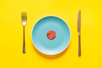Sausage. Sliced smoked sausage on plate with fork and knife isolated on yellow background.