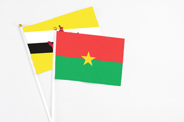Burkina Faso and Brunei stick flags on white background. High quality fabric, miniature national flag. Peaceful global concept.White floor for copy space.