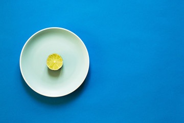 A slice of fresh lime on color plate on blue background with copy space. Flat lay.