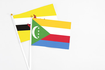 Comoros and Brunei stick flags on white background. High quality fabric, miniature national flag. Peaceful global concept.White floor for copy space.