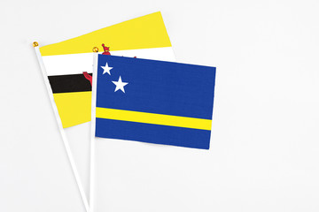 Curacao and Brunei stick flags on white background. High quality fabric, miniature national flag. Peaceful global concept.White floor for copy space.