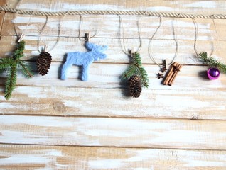 Christmas and new year decoration with fir tree branches, cones, ball, felted woolen moose on pins on rope on wooden background with snow effect