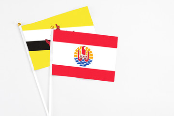 French Polynesia and Brunei stick flags on white background. High quality fabric, miniature national flag. Peaceful global concept.White floor for copy space.