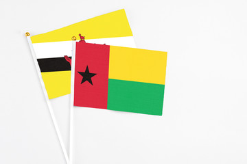 Guinea Bissau and Brunei stick flags on white background. High quality fabric, miniature national flag. Peaceful global concept.White floor for copy space.