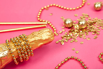 Champagne bottle with golden confetti on pink paper background.