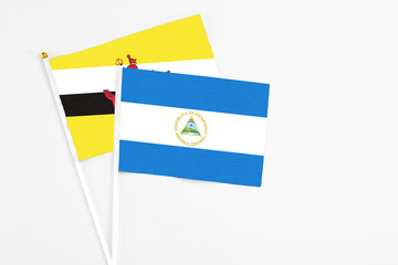 Nicaragua and Brunei stick flags on white background. High quality fabric, miniature national flag. Peaceful global concept.White floor for copy space.