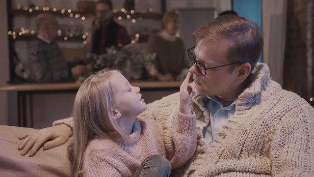 Charming little girl and her young father are talking and smiling while sitting on sofa