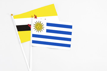 Uruguay and Brunei stick flags on white background. High quality fabric, miniature national flag. Peaceful global concept.White floor for copy space.