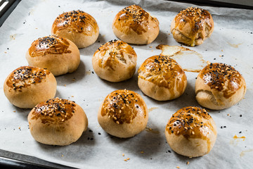Homemade Turkish Pastries Pogaca with Black Cumin and Sesame Seeds on Baking Paper Sheet with Tray.