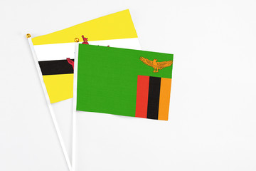 Zambia and Brunei stick flags on white background. High quality fabric, miniature national flag. Peaceful global concept.White floor for copy space.