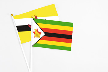 Zimbabwe and Brunei stick flags on white background. High quality fabric, miniature national flag. Peaceful global concept.White floor for copy space.