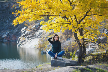 Young woman under yellow tree on lake background.