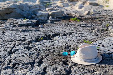 A straw hat and glasses lie on a rock on the beach.Horizontally.