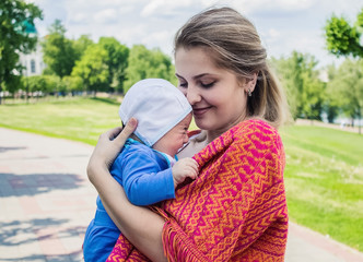 A young girl is holding a baby in her arms.  Mom and son are walking in the park.