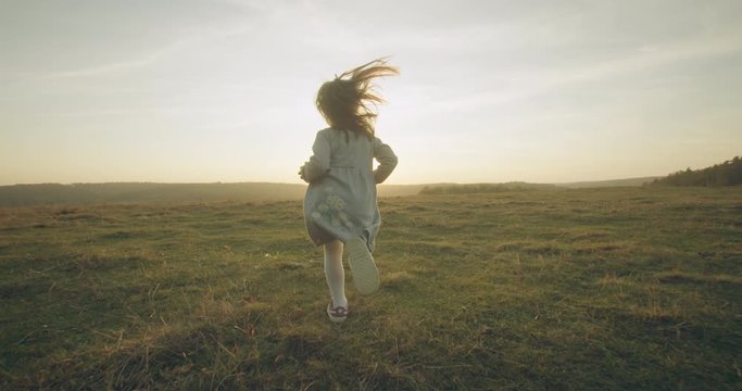 A little girl is running through the autumn field against the background of the sun. Young family on a walk. 4K 