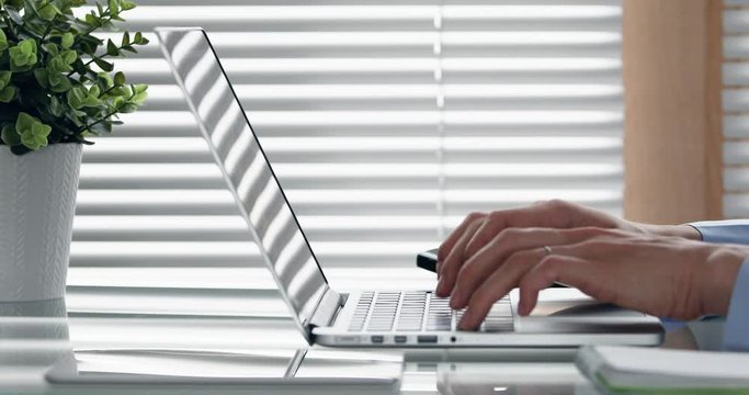 Person typing on computer keyboard in modern office, close-up of business woman hands using laptop on glass table, dolly shot, 4k footage